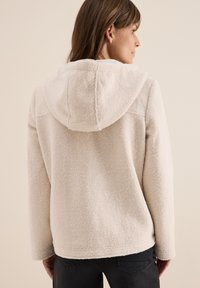 Veste en polaire couleur crème avec une finition douce et texturée, dotée d'une capuche et de manches longues, vue de dos.