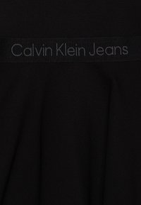 Czarna tkanina z czarnym elastycznym paskiem, na którym wyhaftowany jest szary tekst "Calvin Klein Jeans".