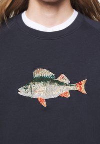 Sudadera azul marino oscuro con un diseño detallado de un pez bordado en tonos verdes, blancos y naranjas, con acentos de costura texturizada.