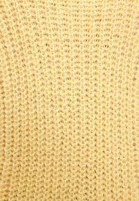 Tissu tricoté en jaune pâle, présentant des points lâches et texturés. Apparence douce avec un motif uniforme.