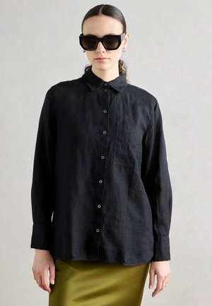 Zwarte linnen shirt met een kraag, lange mouwen en knoopsluiting aan de voorkant; heeft een borstzak en een ontspannen pasvorm.