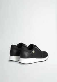 Sneaker nere con dettagli in oro, tessuto testurizzato sulla parte superiore, accentuazioni in pelle liscia e suole in gomma bianca. La vista posteriore mostra il design con lacci.