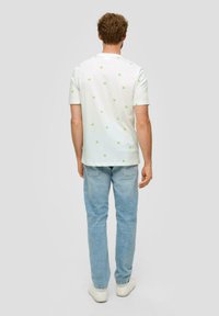 Biała koszula z krótkim rękawem z małymi zielonymi gwiazdkami, w połączeniu z jasnoniebieskimi dżinsami i białymi trampkami, widziana od tyłu.