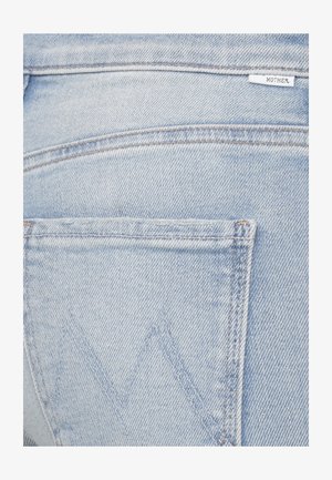 Tasca posteriore di jeans in denim azzurro chiaro con cuciture visibili e una piccola etichetta bianca con la scritta "MOTHER" vicino alla cintura.