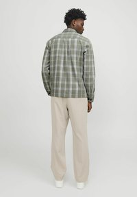 Groene geruite blouse met een knoopsluiting, voorzien van lange mouwen en een comfortabele pasvorm, gecombineerd met beige broeken en witte sneakers.