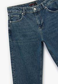 Jeans de mezclilla en un lavado oscuro con corte recto. Presenta un cierre de botón, diseño de cinco bolsillos y costuras visibles.