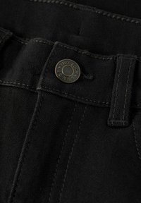 Schwarze Denim-Jeans mit einem sichtbaren Bund, verstärkten Nähten und einem markierten Metallknopf, auf dem "TWO SOON JEANS" steht.