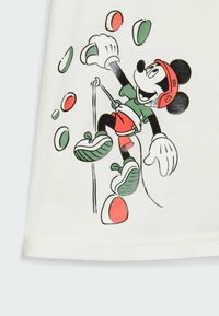 T-shirt bianco in cotone con una grafica di Topolino che scala, vestito in abbigliamento verde e rosso, con prese di arrampicata colorate sopra.