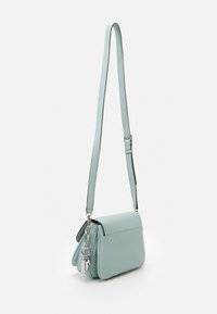 Světle mátově zelená kožená crossbody taška se stříbrným kováním, texturovaným povrchem a magnetickým uzávěrem; má nastavitelný popruh.