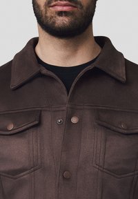 Brązakowa, teksturowana kurtka z kołnierzem, przednimi kieszeniami i kontrastowymi brązowymi guzikami; posiada pionowe detale w postaci przeszyć.