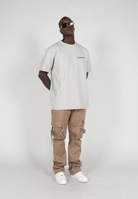 Light grey t-shirt with black text on the chest, paired with tan cargo pants featuring side pockets, and white sneakers. Sunglasses included.