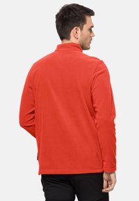 Pullover in pile rosso con colletto alto, maniche lunghe e orlo dritto. Texture morbida con cuciture minime e senza hardware visibile.