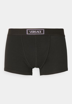 Black boxer shorts with a snug fit, featuring a contrasting white Versace logo on a black waistband. Soft fabric with seamless design.