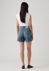 Vaaleansiniset denim-shortsit, joissa on korkea vyötärö ja reikäytyneet saumat. Takakatsauksessa näkyy kaksi takataskua ja brändilappu vyötärön lähellä.