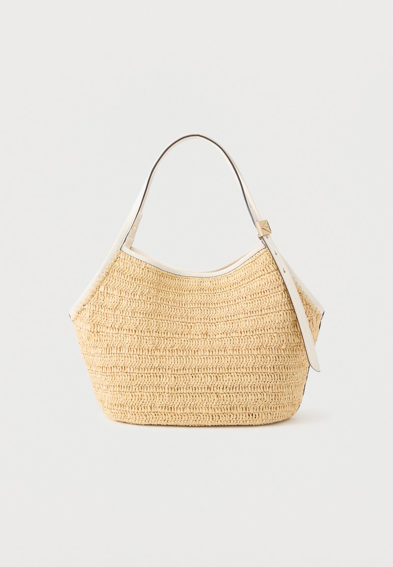 Μπεζ πλεκτή τσάντα από άχυρο με λευκή δερμάτινη επένδυση και ρυθμιζόμενο ιμάντα ώμου, σε απλό φωτεινό φόντο.