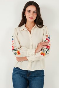 Camisa crema de botones, con coloridos bordados florales en las mangas, hecha de un tejido suave, con corte relajado y mangas con puños.