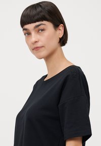 Svart kortermet t-skjorte med rund hals og teksturede skulderdetaljer. Mykt stoff, avslappet passform og minimalistisk design.