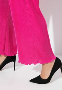 Pantalones de pierna ancha fucsia con plisados y dobladillo festoneado, combinados con unos elegantes tacones altos de ante negro. Textura suave y contraste de color vibrante.