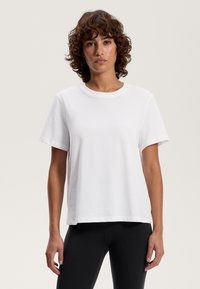 Hvid bomulds t-shirt med rund halsudskæring og korte ærmer, med en afslappet pasform og lige kant. Båret med sorte leggings.