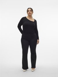 Zwarte geribbelde top met lange mouwen en een asymmetrische halslijn, gecombineerd met aangesloten zwarte jeans en crèmekleurige pumps met puntige neus.