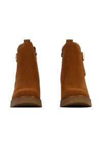 Bottines en daim beige avec une finition lisse, dotées d'une boucle sur le côté et d'un talon bas pour plus de stabilité. Design à bout arrondi.
