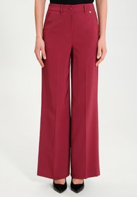 Breda byxor i vinröd tyg med en slät textur, som har en framknapp, bältesloopar och en diskret logodetalj på midjebandet.