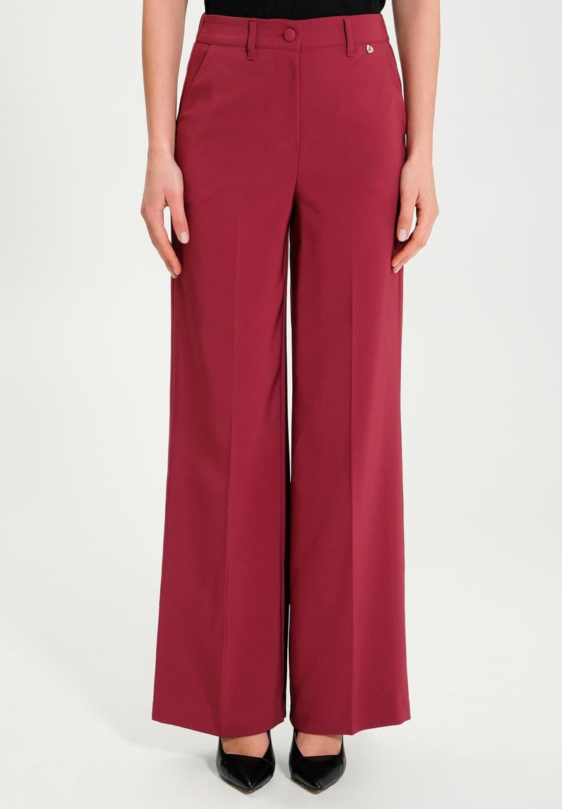 Breda byxor i vinröd tyg med en slät textur, som har en framknapp, bältesloopar och en diskret logodetalj på midjebandet.