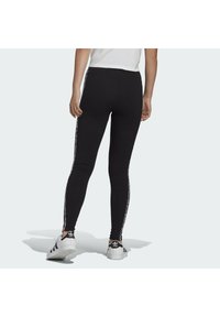 Svarta leggings med en mjuk tygtyp, avsmalnande design och färgglada sidostripes. Kombineras med vita sneakers med svarta detaljer.