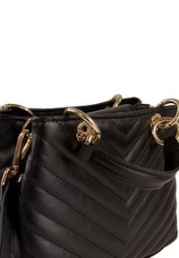 Sac à main en cuir noir présentant un motif chevron, des accessoires dorés, des doubles anneaux et une seule bandoulière pour le porter. Texture lisse.