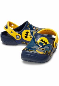 Sabots bleus et jaunes en matériau léger, ornés de motifs Batman, avec des découpes circulaires et des sangles au talon réglables pour le confort.