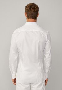 Camicia bianca a maniche lunghe con colletto classico, polsini con bottone, texture liscia e vestibilità tailored, mostrata da dietro.