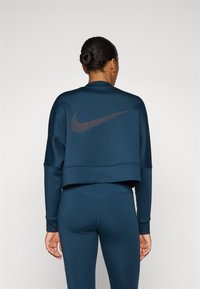 Sweatshirt court bleu marine avec un grand logo noir Nike dans le dos, coutures à plat et texture douce. Associé à des leggings assortis.