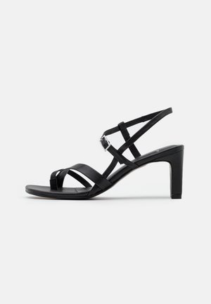 Czarna sandał z wysokim obcasem, z cienkimi krzyżującymi się paskami i zapięciem na klamrę. Charakteryzuje się elegancką, gładką teksturą oraz skromnym obcasem w kształcie bloku.