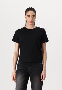 Sort kortærmet t-shirt lavet af blødt bomuld. Har en klassisk rund hals og en afslappet pasform. Bæres sammen med mørkegrå jeans.