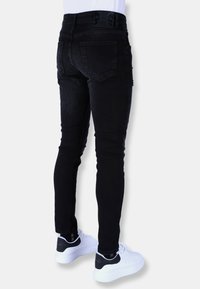 Zwarte skinny jeans gemaakt van denim, met een hoge taille, twee achterzakken en subtiele vervaging. Gepaard met witte sneakers.