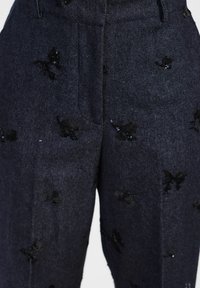Pantaloni in denim scuro caratterizzati da intricate applicazioni di farfalle ricamate in nero e delicati paillettes, con una vestibilità classica e tasche frontali.
