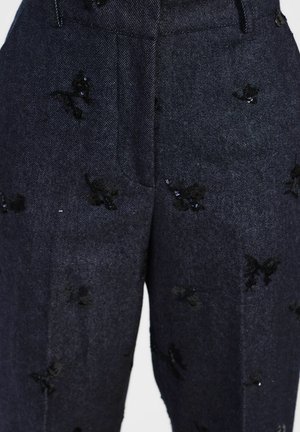 Pantaloni in denim scuro caratterizzati da intricate applicazioni di farfalle ricamate in nero e delicati paillettes, con una vestibilità classica e tasche frontali.