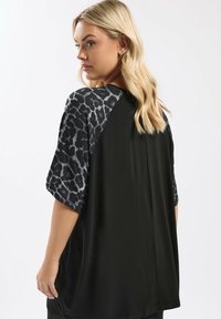 Schwarzes Kurzarmoberteil mit Leo-Musterakzenten an den Ärmeln, mit lässigem Schnitt und weichem Material.