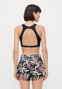 Svart sportsbh med utskjært bakside og justerbar hardware, kombinert med shorts med blomsterprint i mørke farger, med rosa og grønne aksenter.