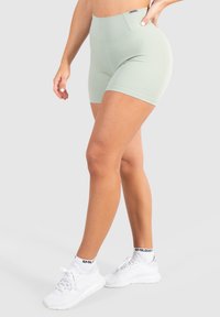 Shorts verde menta realizzati in un tessuto elasticizzato con vita alta. Presentano un design minimale e una forma aderente, abbinati a sneakers bianche.