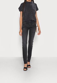 Sort glitrende kortærmet top med tætsiddende silhuet. Sæt sammen med sorte skinny jeans med forlommer. Bærer med sorte open-toe stilethæle.
