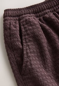 Fioletowe spodnie o fakturze z elastycznym pasem i bocznymi kieszeniami, zdobione wypukłym okrągłym wzorem na powierzchni tkaniny.