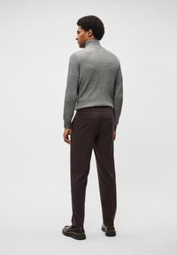 Camisola cinza de gola alta com nervuras, combinada com calças castanho-escuras. O conjunto apresenta texturas subtis e um ajuste casual, complementado por sapatos de couro macio.