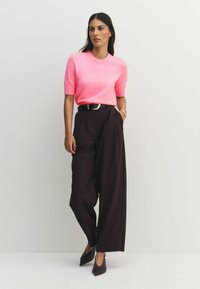 Roza pulover s kratkimi rokavi, kombiniran z visokim pasom in temnimi širokimi hlačami. Vključen je črni pas z zlatim zaponko in čevlji z ostro konico.