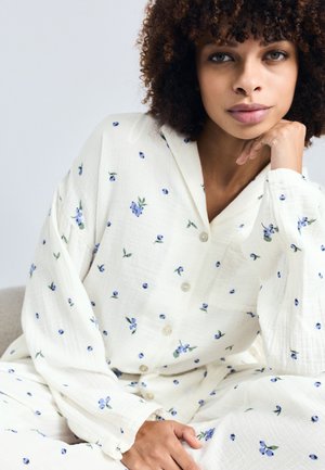 Vit skjorta med blå blommönster, lång ärm och avslappnad passform. Har krage och mjukt, texturerat tyg.