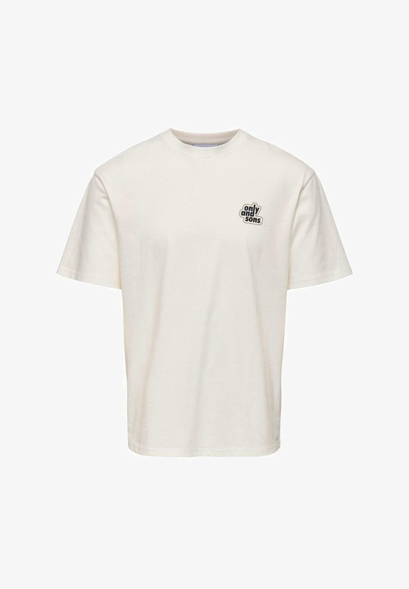 T-shirt à manches courtes en coton crème avec un col rond et un petit patch logo noir sur la poitrine gauche. Design simple, sans motifs.