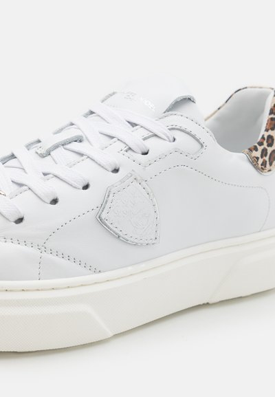 Sneaker in pelle bianca con lacci bianchi, crest in rilievo sul lato e dettagli in stampa leopardata sul colletto del tallone.