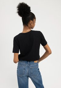 T-shirt en coton noir à col rond et manches courtes, associé à un jean en denim bleu taille haute avec deux poches arrière et une étiquette.