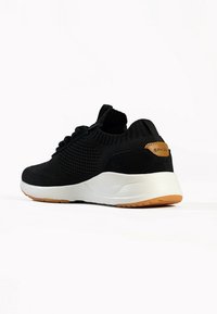 Black knit sneaker featuring a white midsole and gum outsole. Includes textured detailing and a small brown leather accent on the heel.