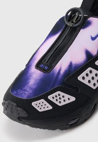 Sapatilha preta e roxa com um upper texturizado, fecho de zíper, detalhes perfurados e uma etiqueta "AIR" em destaque perto do topo.